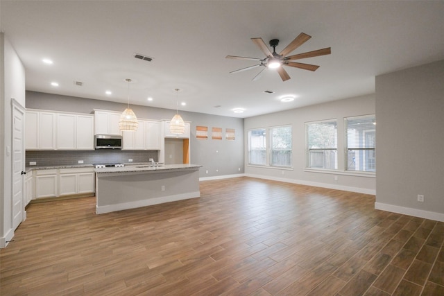 kitchen with white cabinets, hanging light fixtures, a kitchen island with sink, and decorative backsplash