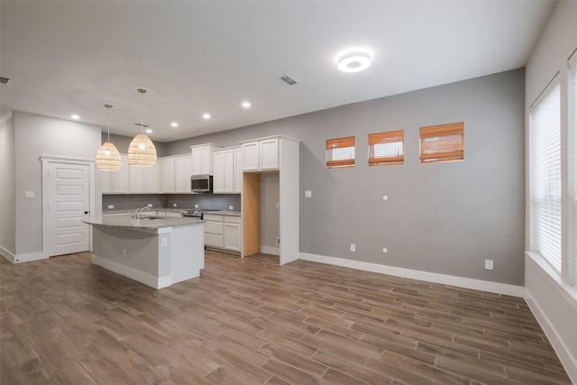 kitchen with white cabinetry, decorative backsplash, stainless steel appliances, light stone counters, and a center island with sink