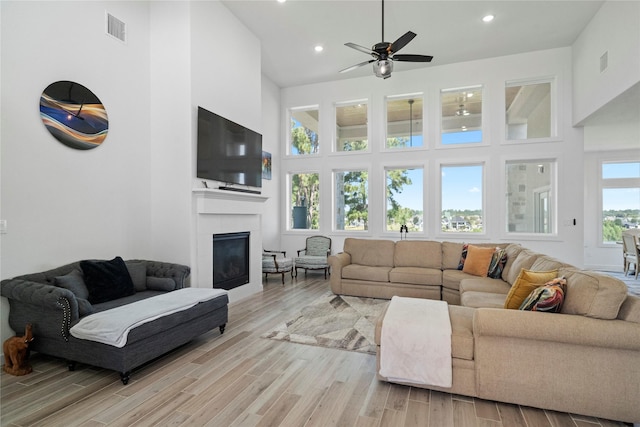 living room with a towering ceiling, a wealth of natural light, light hardwood / wood-style floors, and a fireplace