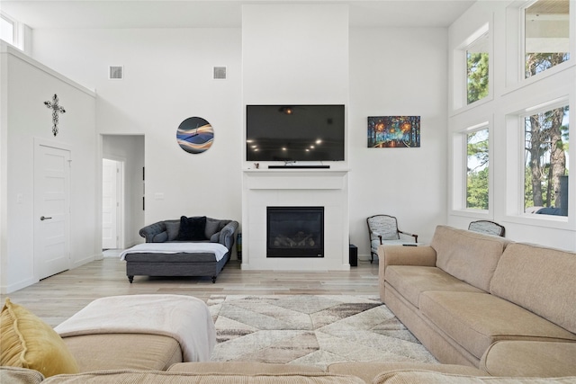 living room with a fireplace, light hardwood / wood-style floors, and a high ceiling