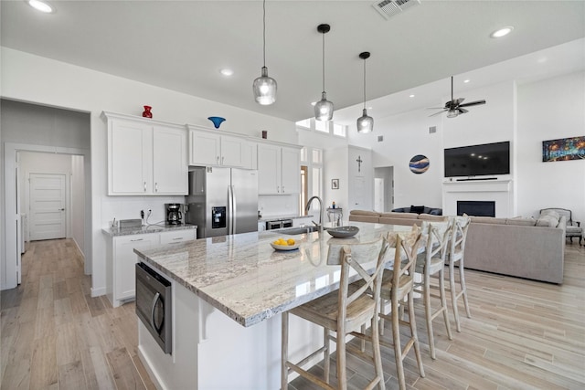 kitchen with light stone countertops, pendant lighting, white cabinets, appliances with stainless steel finishes, and a kitchen island with sink