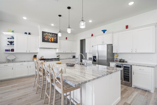 kitchen with stainless steel fridge with ice dispenser, an island with sink, white cabinetry, and light wood-type flooring