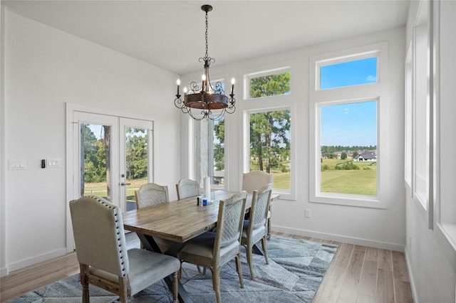 dining space with light hardwood / wood-style flooring, a notable chandelier, and french doors