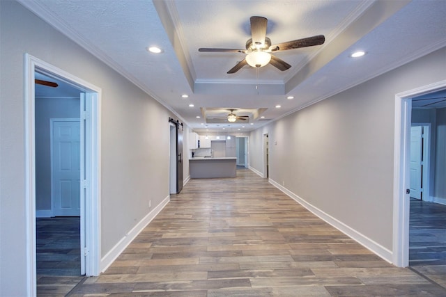 corridor featuring wood-type flooring, a tray ceiling, a barn door, a textured ceiling, and ornamental molding