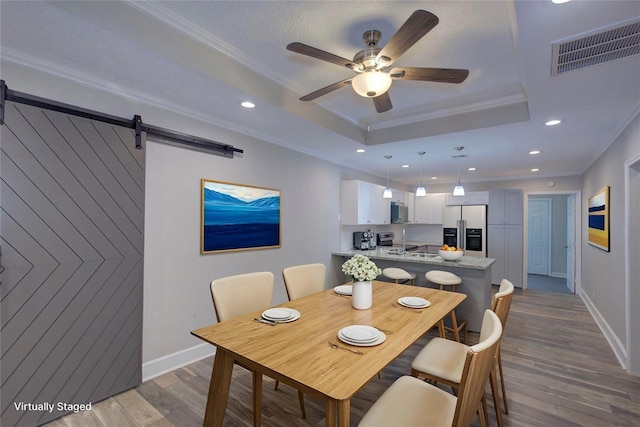 dining area featuring ceiling fan, ornamental molding, hardwood / wood-style flooring, a tray ceiling, and a barn door