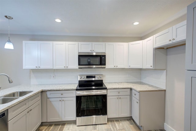 kitchen with appliances with stainless steel finishes, hanging light fixtures, sink, light wood-type flooring, and white cabinets