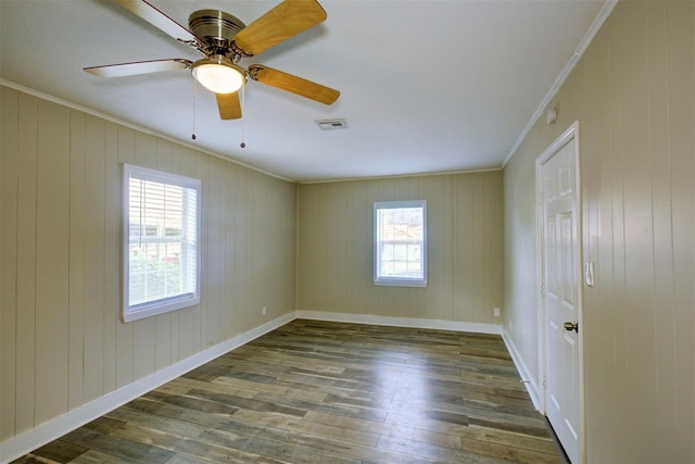 empty room featuring dark wood-type flooring, plenty of natural light, ornamental molding, and ceiling fan