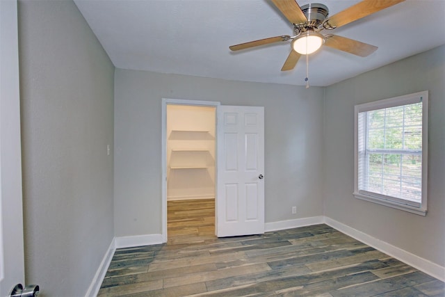 unfurnished bedroom with a spacious closet, a closet, dark hardwood / wood-style flooring, and ceiling fan