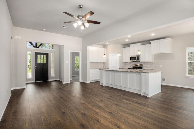 kitchen with light stone counters, white cabinets, stainless steel appliances, and a kitchen island with sink