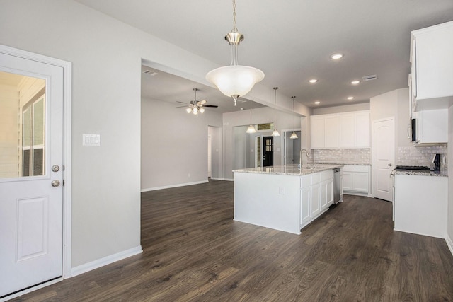 kitchen featuring light stone countertops, pendant lighting, dark wood-type flooring, white cabinetry, and an island with sink