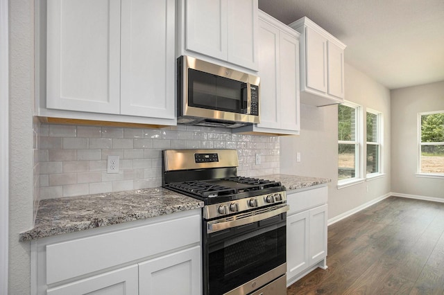 kitchen featuring appliances with stainless steel finishes, backsplash, dark wood-type flooring, white cabinetry, and light stone countertops