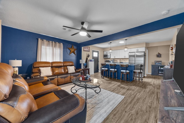 living room with ceiling fan, a healthy amount of sunlight, light hardwood / wood-style floors, and a textured ceiling