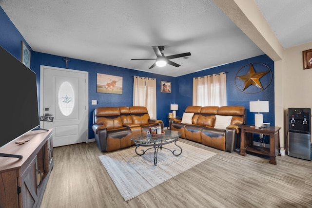 living room with light wood-type flooring, ceiling fan, and a textured ceiling