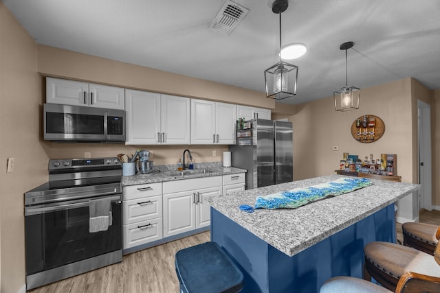 kitchen featuring a kitchen bar, appliances with stainless steel finishes, white cabinetry, sink, and pendant lighting