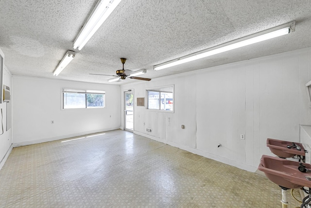 empty room featuring ceiling fan, wood walls, a textured ceiling, and a wealth of natural light