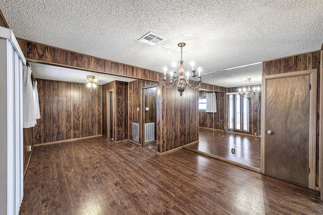 interior space featuring wood walls, an inviting chandelier, a textured ceiling, and dark wood-type flooring