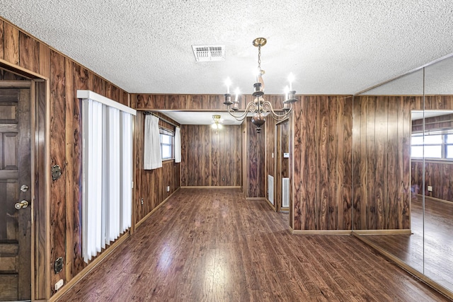 unfurnished dining area with a textured ceiling, dark hardwood / wood-style flooring, a chandelier, and wooden walls