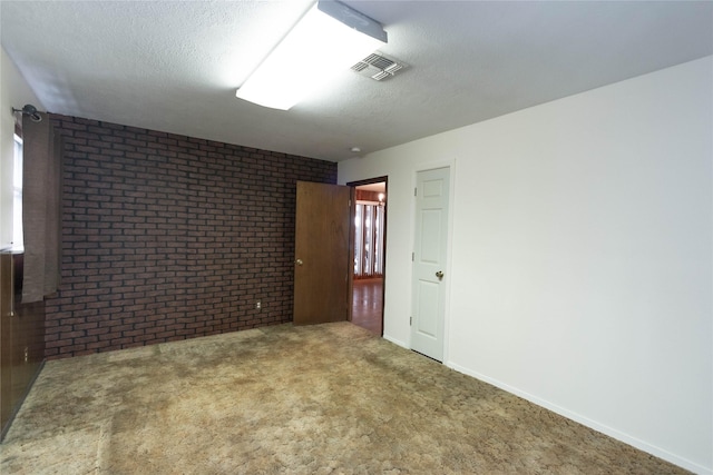 carpeted empty room featuring a textured ceiling and brick wall