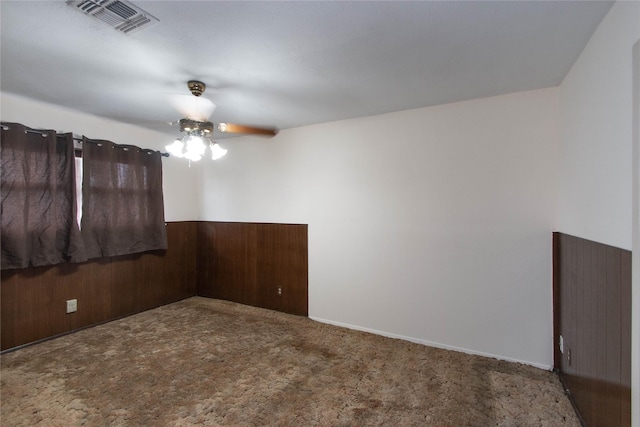 spare room featuring ceiling fan, wood walls, and carpet