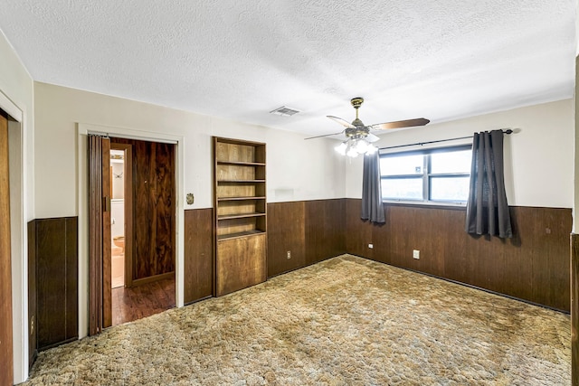 spare room featuring carpet floors, a textured ceiling, ceiling fan, and wooden walls