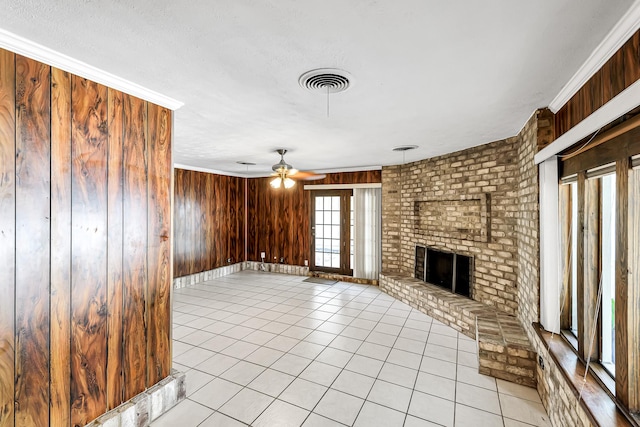 unfurnished living room featuring a fireplace, wooden walls, ceiling fan, light tile patterned floors, and crown molding