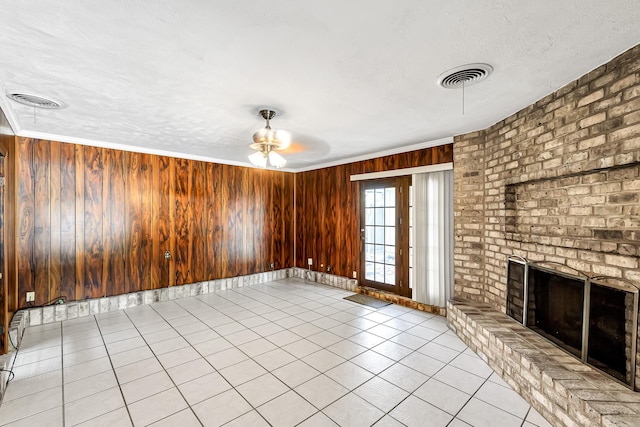 unfurnished living room featuring crown molding, a textured ceiling, a brick fireplace, light tile patterned floors, and wood walls