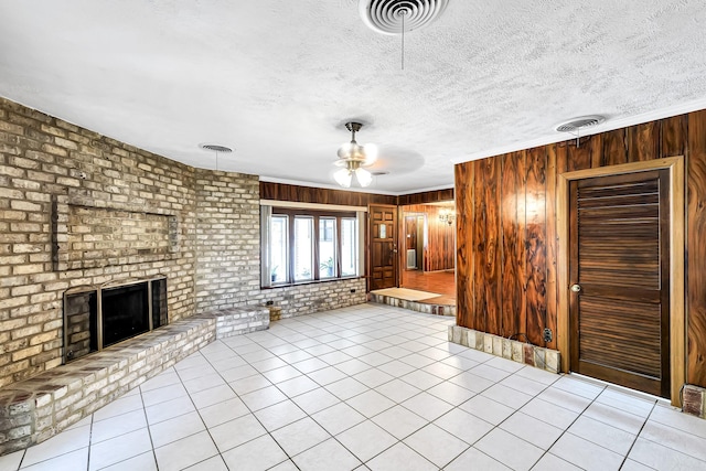 unfurnished living room with ceiling fan, light tile patterned flooring, wooden walls, and a brick fireplace