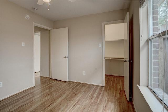 unfurnished bedroom featuring light wood-type flooring, ceiling fan, a spacious closet, and a closet