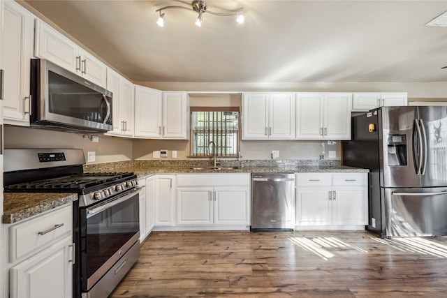 kitchen with light hardwood / wood-style flooring, sink, white cabinetry, dark stone countertops, and stainless steel appliances