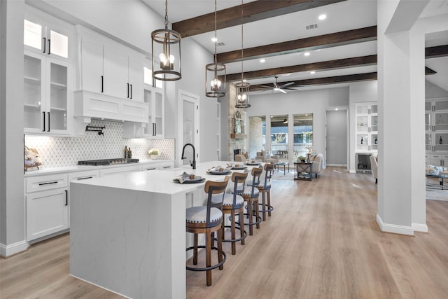 kitchen with premium range hood, decorative light fixtures, white cabinets, stainless steel gas cooktop, and a center island with sink