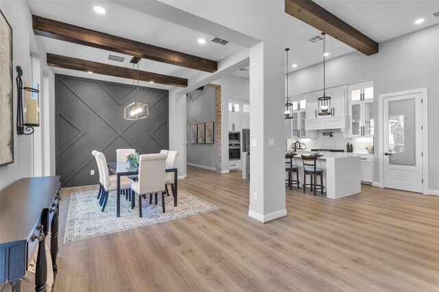 dining space featuring an inviting chandelier, beamed ceiling, and light wood-type flooring