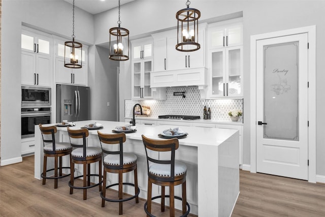 kitchen with hanging light fixtures, a kitchen island with sink, white cabinetry, and stainless steel appliances