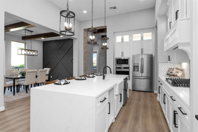 kitchen featuring pendant lighting, appliances with stainless steel finishes, white cabinets, a barn door, and a kitchen island with sink