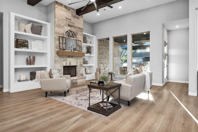 living room featuring ceiling fan, a fireplace, light hardwood / wood-style floors, and beam ceiling