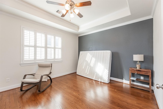 living area with wood-type flooring, ornamental molding, ceiling fan, and a raised ceiling