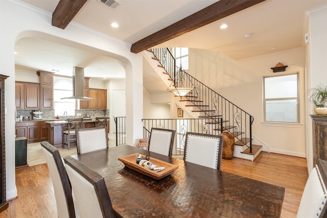 dining area featuring sink, beam ceiling, light hardwood / wood-style floors, and crown molding