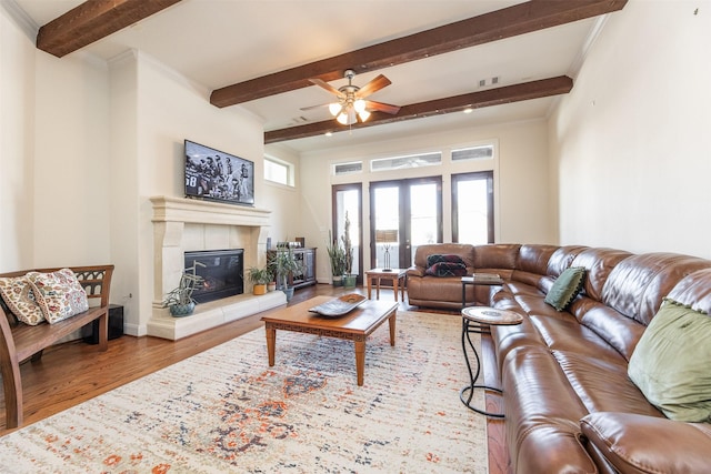 living room with beamed ceiling, wood-type flooring, french doors, a tiled fireplace, and ceiling fan