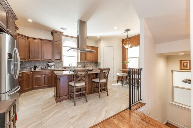 kitchen featuring a center island, a kitchen bar, island exhaust hood, decorative backsplash, and stainless steel refrigerator with ice dispenser