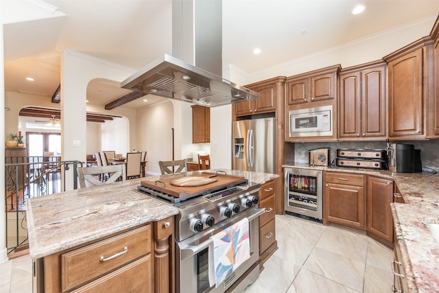 kitchen with light stone countertops, island exhaust hood, beverage cooler, and appliances with stainless steel finishes