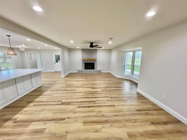 unfurnished living room with ceiling fan, light wood-type flooring, and a brick fireplace