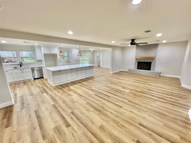 unfurnished living room with a brick fireplace, sink, light hardwood / wood-style flooring, and ceiling fan