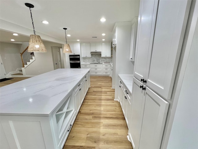 kitchen featuring white cabinetry, light hardwood / wood-style flooring, a spacious island, and light stone counters