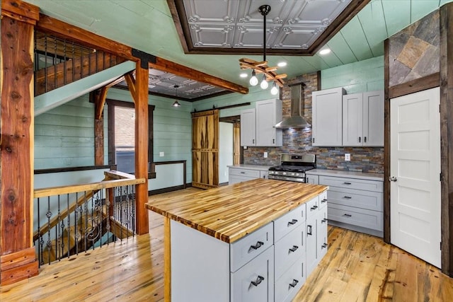 kitchen with gas range, wall chimney range hood, decorative light fixtures, white cabinets, and wood counters