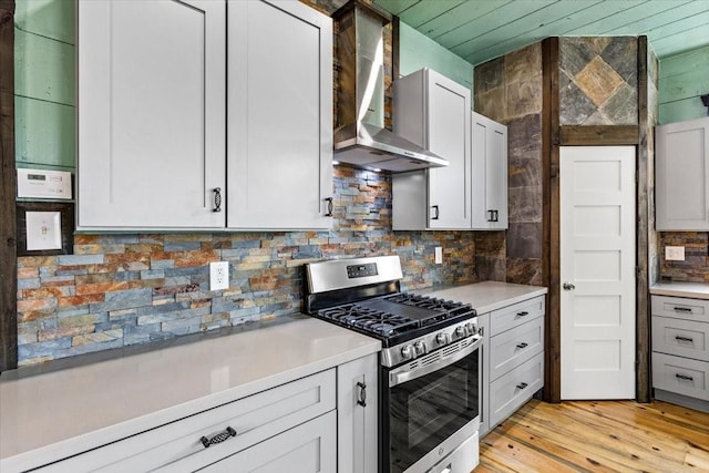 kitchen with stainless steel gas stove, white cabinets, tasteful backsplash, wall chimney range hood, and light hardwood / wood-style floors