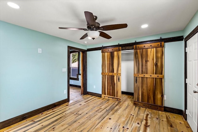 unfurnished bedroom with ceiling fan, a closet, a barn door, and light wood-type flooring