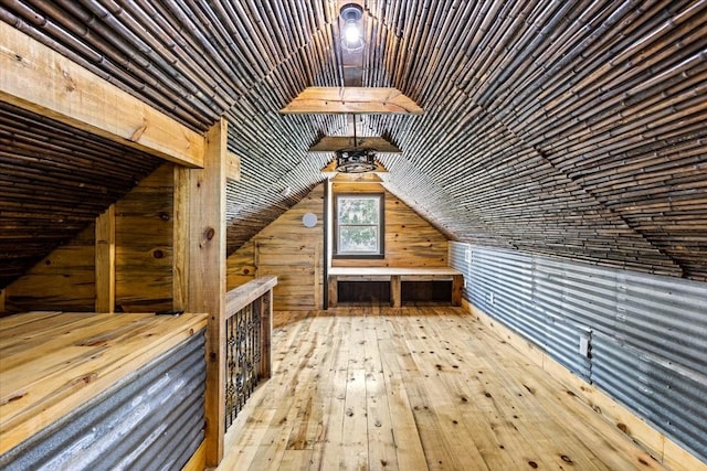 additional living space featuring light wood-type flooring, wooden walls, and lofted ceiling