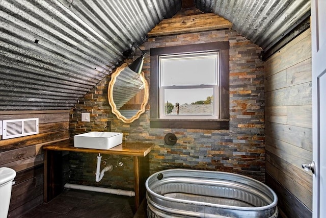 bathroom featuring tile patterned flooring, vaulted ceiling, sink, toilet, and wood walls