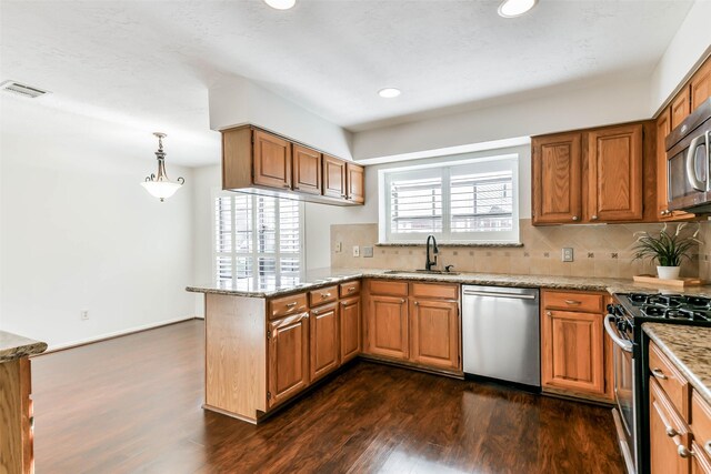 kitchen featuring dark wood-type flooring, stainless steel appliances, sink, hanging light fixtures, and kitchen peninsula