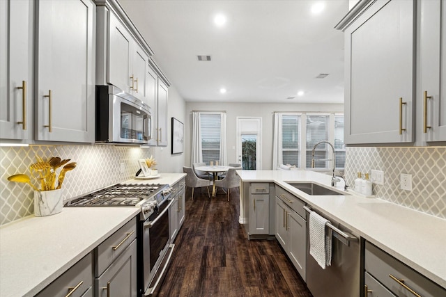 kitchen with sink, dark wood-type flooring, gray cabinetry, decorative backsplash, and stainless steel appliances