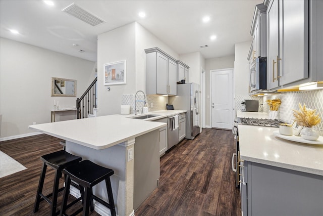 kitchen with appliances with stainless steel finishes, decorative backsplash, sink, kitchen peninsula, and gray cabinets